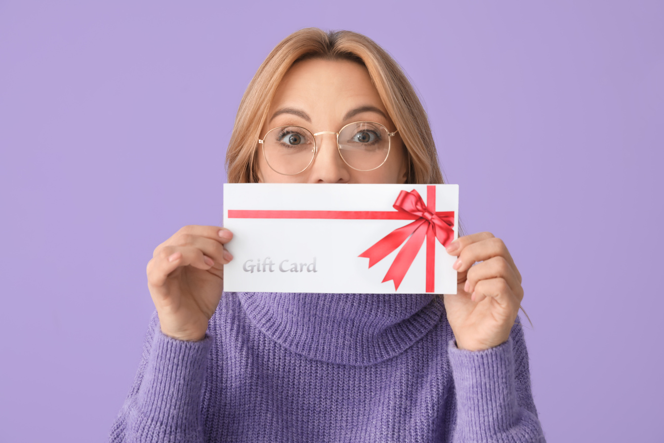 Mature Woman with Gift Card on Color Background